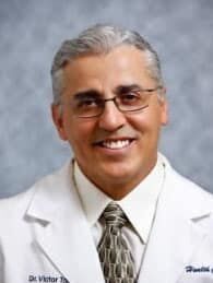 Dr. Victor Torres, DC Headshot photo of Dr. Victor Torres, chiropractor at Eustis Injury Medical Center: Lake Health Care Center, wearing glasses, a dress shirt, tie and medical jacket with his name embroidered on the right chest panel and "Lake Health Care Center" on the left chest panel.