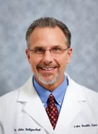 Dr. Heiligenthal, Jr., DC Headshot photo of Dr. John Heilegenthal, Jr., chiropractor at Eustis Injury Medical Center: Lake Health Care Center, wearing glasses, a dress shirt, tie and medical jacket with his name embroidered on the right chest panel and "Lake Health Care Center" on the left chest panel.