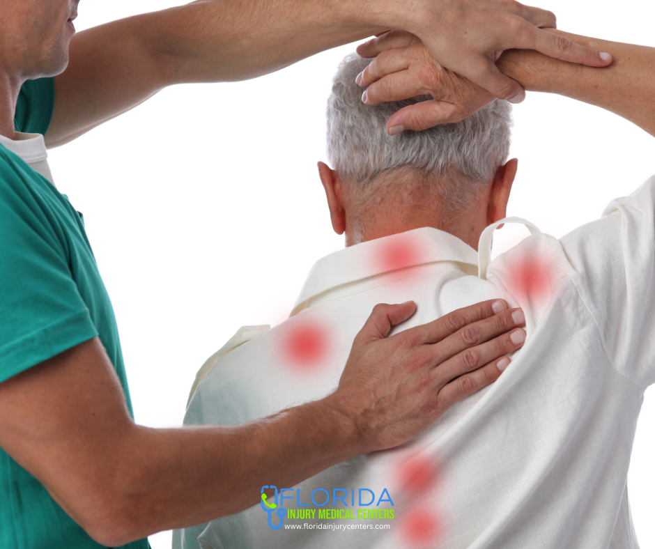 picture of the back of an older man with his right arm bent at the elbow and his right hand on the back of his head, while a chiropractor has his right hand on the middle of the patients upper back and his left hand holding the patient's right hand. There are red dots along the patient's shirt to represent trigger point therapy.