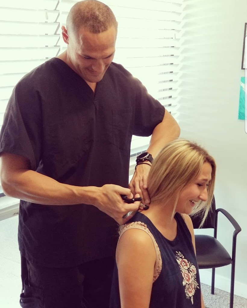 Dr. Havlicek standing behind a female patient, using an Activator on her neck along the cervical spine.