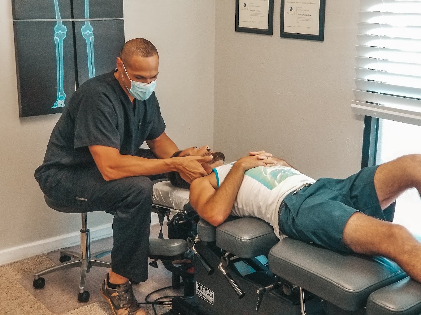 Dr. Havlicek sitting near the head of a male patient that is laying on an adjustment table. Doctor has his hands on both sides of the patient's head, performing an adjustment.