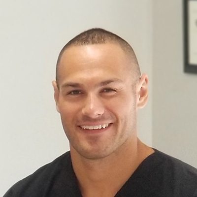 Heashot photo of Dr. Bradley Havlicek, chiropractor at St Augustine Medical Injury Center: Havlicek Chiropractic, smiling and wearing a black scrub shirt.