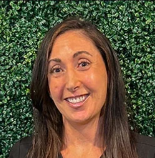 Heashot photo of Dr. Beth West, chiropractor at Tallahassee Medical Injury Center: Balanced Chiropractic, smiling and standing in front of a wall of greenery.