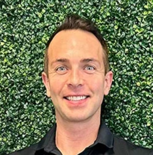 Heashot photo of Dr. Kory Johnson, chiropractor at Panama Citty Medical Injury Center: Balanced Chiropractic, smiling and standing in front of a wall of greenery.