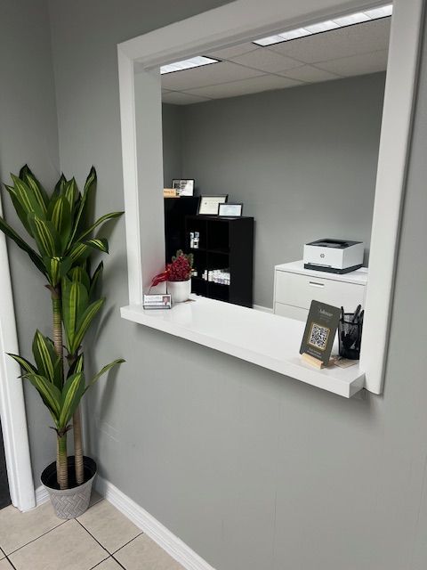 View of reception desk which is a square opening through wall with counter in foreground an office on opposite side.