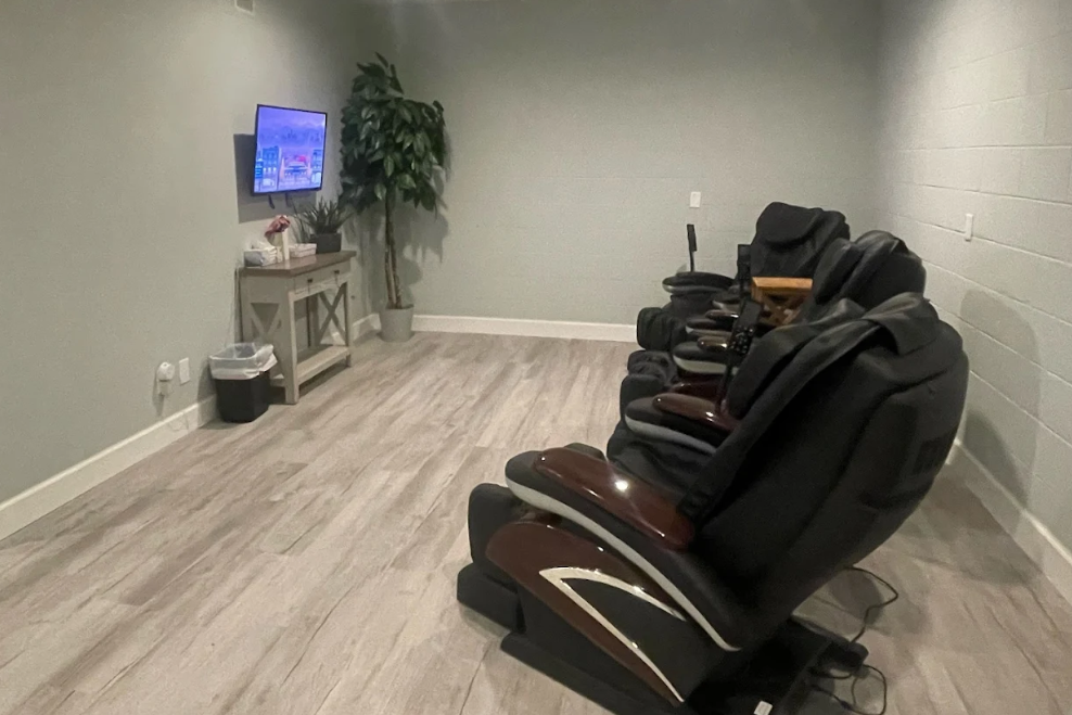 View of a room with three massage chairs along a wall with a tv on the opposite side of the room at Balanced Chiropractic in Tallahassee, Florida.