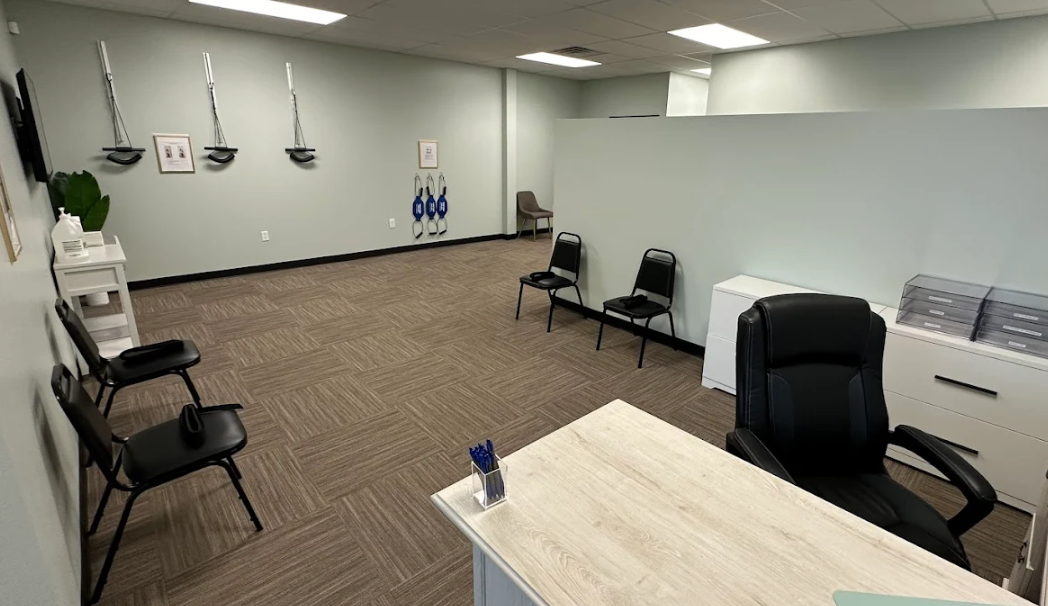 Therapy room with neck stretcher tools on one wall, a desk in the foreground and a couple of straight chairs in front of a half wall at Panama City Medical Injury Center: Balanced Chiropractic
